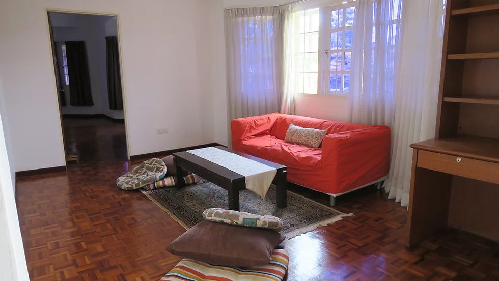 Living room with red sofa, dark wood coffee table, striped floor cushions, parquet flooring, light curtains, cozy casual