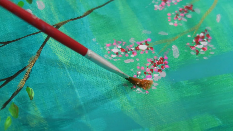 Close-up of a paintbrush adding pink and white dot details to a teal-colored painting, artistic and creative mood